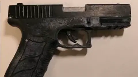 A black handgun, set against a beige background.