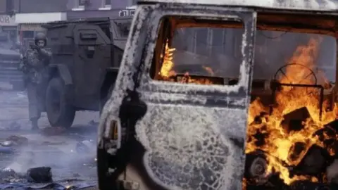 Getty An armed British Army soldier walks toward a burning van beside a large armoured vehicle