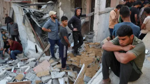 A man sits as Palestinians gather at the site of an Israeli strike on a house in Gaza. 