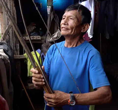 Juan is wearing a blue T-shirt and holding a bow 