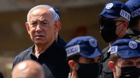 Getty Images Netanyahu looks on while surrounded by police officers with caps on while standing outdoors at the site of a strike in Dimona, Israel on Sunday.