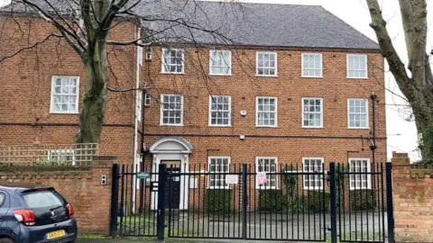 A large red brick building with white sash windows and black gates in front. 