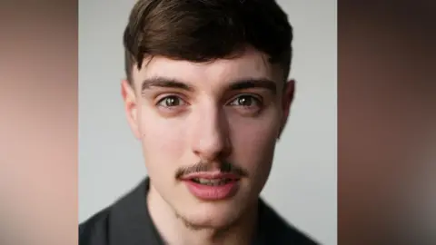 Chris Mann A headshot image of a man with brown hair, a floppy fringe and a grey polo short is smiling at the camera