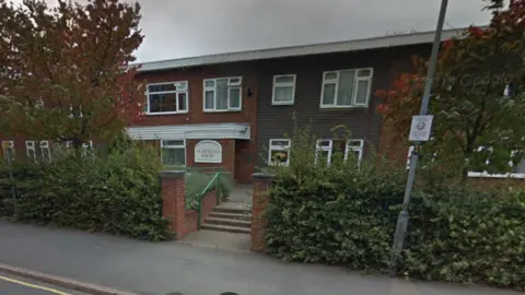 Google Housing which has the sign St Michael's Court behind a lamp post. There are also bushes and trees in front of the houses