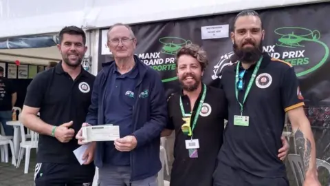 Allan Brew Allan Brew posing with three men. He is holding a cheque which will be given to the riders.