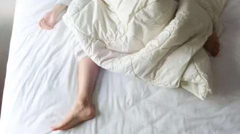 Getty Images Person in bed with a duvet partly thrown off them