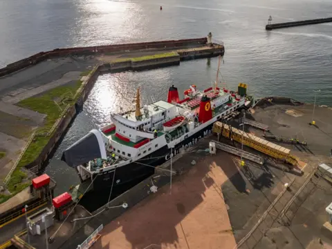 Stewart McGookin A black and white ship with red funnels berthed at a harbour. The harbour wall