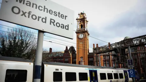 EPA-EFE/REX/Shutterstock Tanda bertuliskan 'Manchester Oxford Road' di depan kereta api dan menara jam yang tinggi dan sempit di stasiun Manchester Oxford Road.