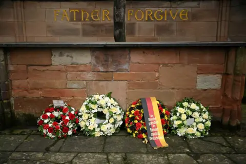 Reuters Four floral wreaths placed in front of the altar of Coventry Cathedral ruins. One bears the colours of Germany's flag. Above the altar the words "Father Forgive" can be seen. 