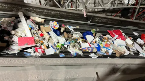 Lots of rubbish on a conveyor belt including crisp packets and bits of card