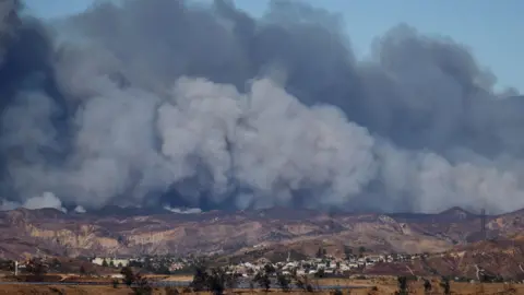 Smoke plumes can be seen billowing in the sky near communities in Los Angeles county 