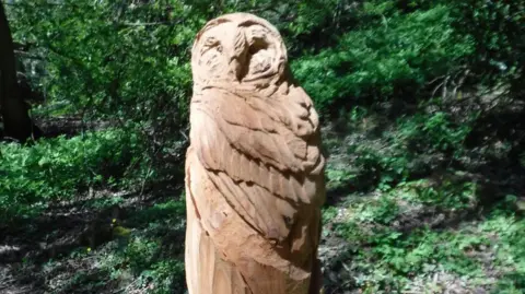 National Highways A wooden chainsaw sculpture of an owl in a woodland area.
