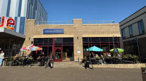 Jordan Harries The outside of a restaurant can be seen with outdoor seating in the foreground. On the left, there is a Vue cinema entrance.