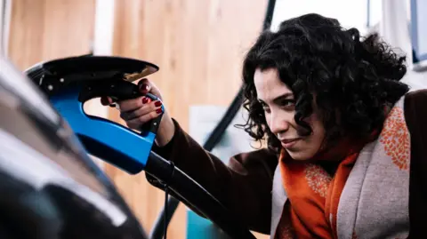 Woman with dark hair plugs in electric vehicle to charging point