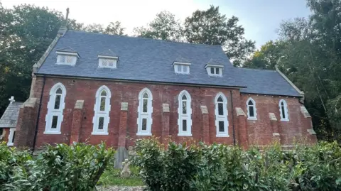 The exterior of a Grade II listed, showing the new white PVC windows added to the red brick church building.