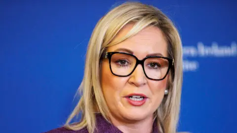 PA Media Shows a woman with blond hair, dark rimmed glasses and a purple jacket 
