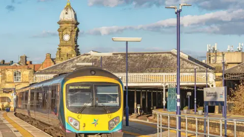 Picture showing a train pulling out of Scarborough Railway Station, in the background there is the historic clock tower. 