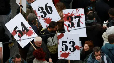 Reuters People holding white placards with red splodges and numbes 54, 53 and 37 to remember the dead