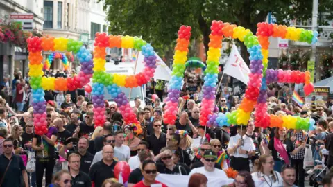 Getty Images Pride Cymru supporters parade through the city centre in Cardiff. Rainbow balloons spell PRIDE and attendees line the streets. 