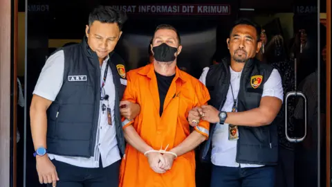 EPA Lyons has his hands tied together as he is led from the detention centre by two officers