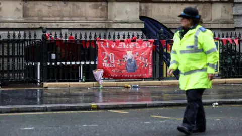 A police officer walks past a Liverpool FC flag at the site of an incident where a car ploughed into a crowd of Liverpool fans during a parade celebrating their side's Premier League title