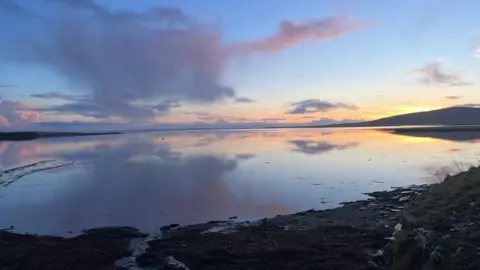 A bay with a sunset and rocks in the foreground.