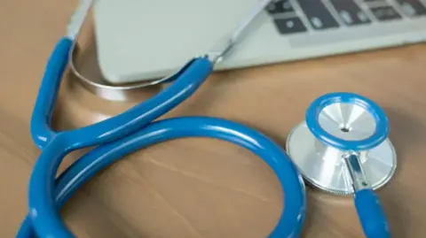 A blue stethoscope next to a laptop computer on a wooden table.