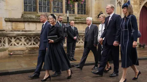 PA Media Lord Tebbit's three children walking down a street outside the cathedral holding hands with their partners. Behind them are two members of staff.
