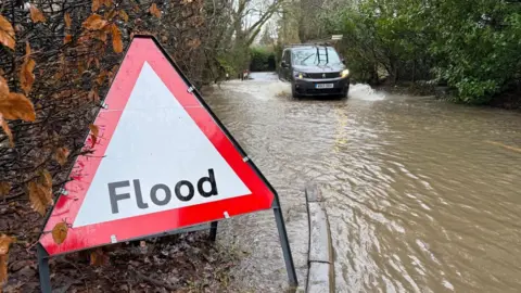 Eddie Mitchell A red flood sign. Behind it, a van is driving. 