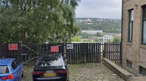 Two cars parked in front of a fence overlooking an embankment with a view over the city