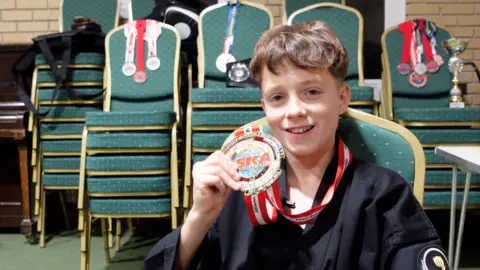 Seb smiles directly into the camera holding his gold medal