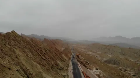 Getty Images A road running between brown, barren hills in Balochistan as the landscapestretches endlessly on either side 