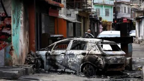 Reuters A person looks on behind a burnt car during a police operation against drug trafficking at the favela do Penha, in Rio de Janeiro