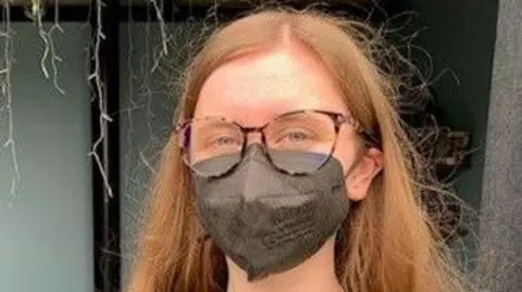 Seren, a girl with red hair and glasses wearing a respirator mask