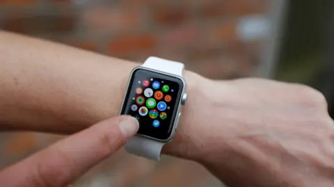 PA Media Close up of an Apple Watch with a white strap on a person's wrist, with their index finger tapping the screen