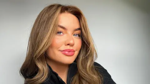 Selfie of Olivia McVeigh smiling to the camera. She has blue eyes and long brown hair. 