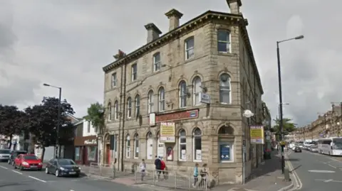 A corner building, with a red sign saying 'Victoria hotel' with people walking past on the pavement