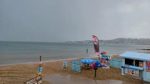 BBC Weather Watcher, LordReith Swanage beach, Dorset with a hut on the beach and beach toys in front on a rainy day.