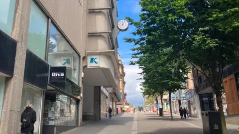 Grace Wood/BBC A view up Darley Street with Kirkgate Centre on the left and Darley Street Market on the right. It is a sunny day there is a tree on the right and a man walking on the left