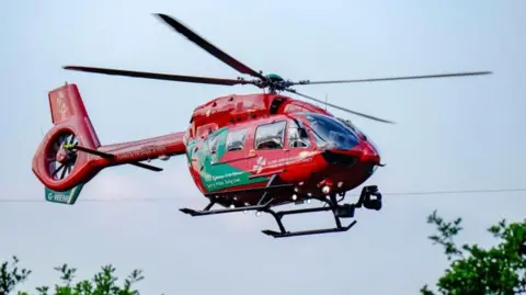Getty Images A red and green helicopter ambulance in the sky, with trees below.