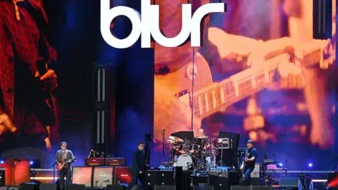 Jim Dyson/Getty Images Blur performing onstage at Wembley under a huge white BLUR sign