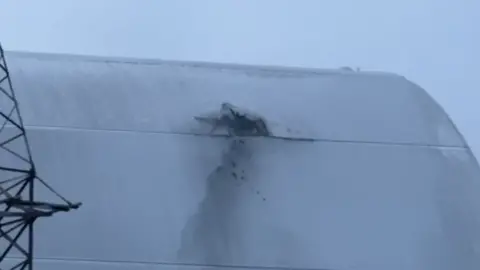 A dark hole in the grey curved shelter that protects Chernobyl's reactor