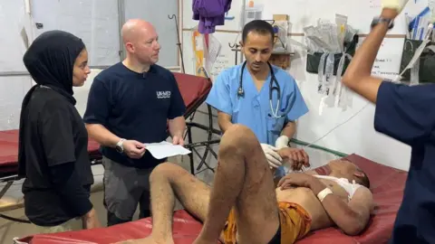 British paramedic Sam Sears (2nd L) observes as an injured Palestinian man receives treatment at the UK-Med field hospital in al-Mawasi, southern Gaza