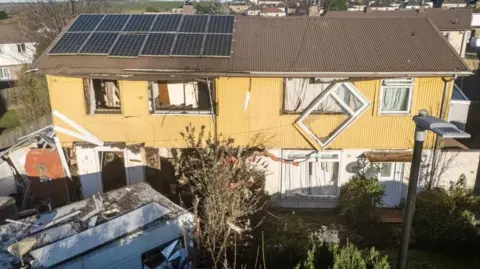 Aftermath of blast at house, with image of windows blown out in two houses and frame hanging off one window.