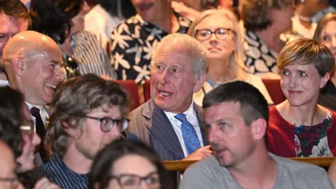 Jeff Spicer via Getty Images King Charles III sits in the audience of a performance of The Tempest at the Royal Shakespeare Theatre.