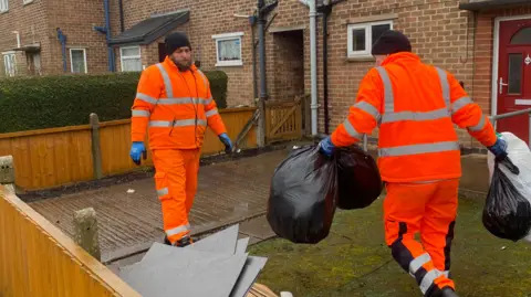 Waste collectors in orange high vis with black bin bags full of waste 