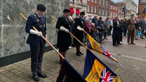 Three military cadets lower flags during a two minutes' silence in Newbury town centre as a crowd of people stand nearby