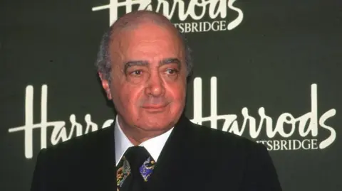 BBC The late former Harrods owner Mohamed Al-Fayed standing in front of the Harrods logo