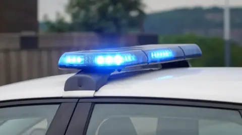 BBC The top of a police car with a blue flashing light.