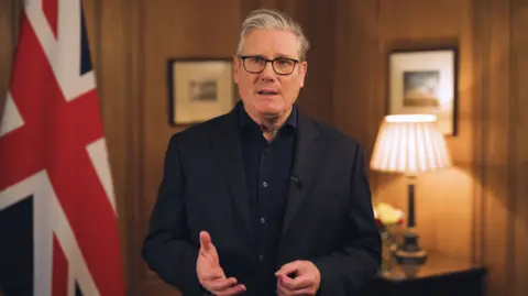 Downing Street Sir Keir Starmer reads his new year's message, standing in a wood-panelled room in front of a Union Jack.